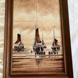 Puede incluir: Una obra de arte enmarcada que representa veleros en el agua. La pintura está en tonos marrones y beige, con los veleros con velas marrones. La obra de arte está enmarcada en un marco de madera marrón oscuro.