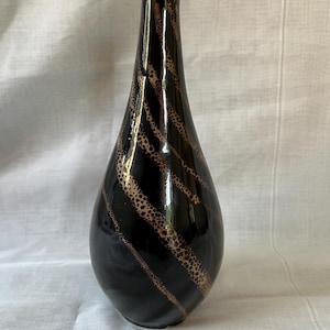 May include: A black ceramic vase with a brown and gold swirl design. The vase has a narrow neck and a rounded body.