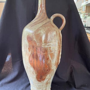 Peut inclure: Une grande jarre en céramique brune et blanche avec une anse. La jarre présente un motif décoratif de losanges avec un motif en spirale sur le devant.