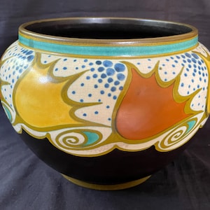 May include: A black ceramic vase with a stylised floral design in yellow, orange, blue, and green. The vase has a wide mouth and a rounded body.