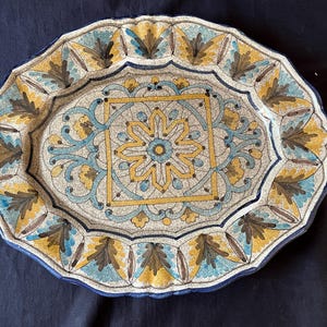 May include: A large, oval ceramic serving platter with a white background and intricate blue, yellow, and brown floral designs. The center of the platter features a large, square, yellow floral design.