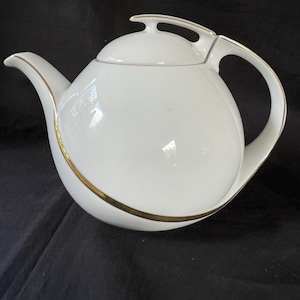 May include: White ceramic teapot with a gold trim around the bottom. The teapot has a rounded body and a curved spout. The lid has a gold handle.