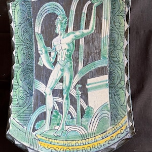 Może przedstawiać: Zielono-biała ceramiczna płytka ścienna z  stylizowanym wizerunkiem postaci trzymającej dzbanek i wlewającej wodę. Płytka ma czarną ramkę i napis "VROKAN 8 - VIII - 1930 GOTEBORG" w kolorze żółtym.