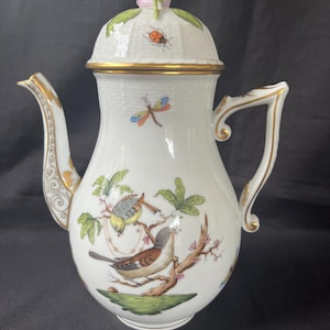 May include: White porcelain teapot with a lid topped with a pink rose. The teapot is decorated with gold trim and hand-painted birds, a dragonfly, and a ladybug. The handle and spout are also trimmed with gold.