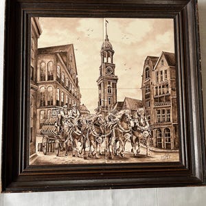 Puede incluir: Arte en azulejo enmarcado en tonos sepia que representa un carruaje tirado por caballos en una calle adoquinada, con edificios y una torre del reloj al fondo. La obra de arte está enmarcada en un marco de madera marrón oscuro.