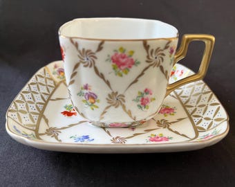 Può includere: Un set da tè in porcellana bianca con un motivo floreale e dettagli dorati. La tazza ha una forma quadrata e un manico. Il piattino ha un bordo ondulato.