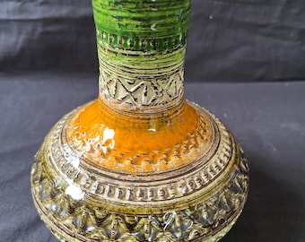 May include: A green, orange, and brown ceramic vase with a textured surface and a wide base.