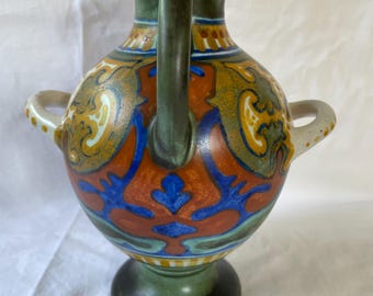 May include: A green and white ceramic vase with two handles and a geometric pattern in shades of orange, blue, and yellow.