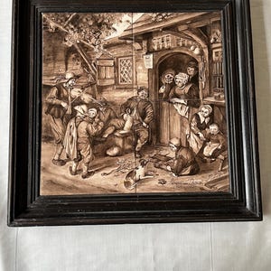 Puede incluir: Una obra de arte en baldosas de cerámica en tonos sepia que representa una escena de taberna con figuras, un perro y un músico. La obra de arte está enmarcada en un marco de madera negro. La escena incluye personas bebiendo y socializando.