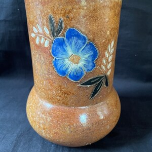 May include: A brown ceramic vase with a blue flower and white and black leaf design.