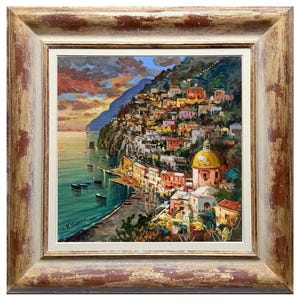 May include: An oil painting of a coastal Italian town, featuring colorful buildings cascading down a hillside to the sea. The artwork is framed in a distressed, gold-toned wooden frame. Boats dot the turquoise water, and the sky displays a sunset.