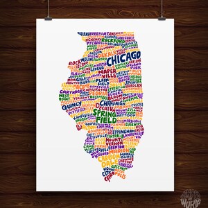 May include: A white poster with a colorful map of Illinois, USA, composed of city names. The state outline is filled with text in various colors, including Chicago, Springfield, and Peoria. The poster is hanging on a wooden wall.