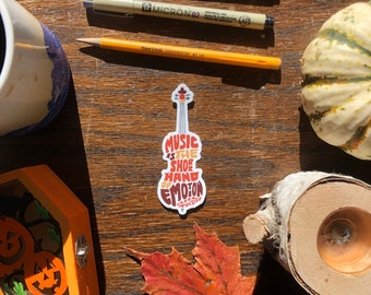 May include: A white sticker with a violin outline and the text "Music is the shoe hand of emotion Tolstoy" in orange, red, and yellow.