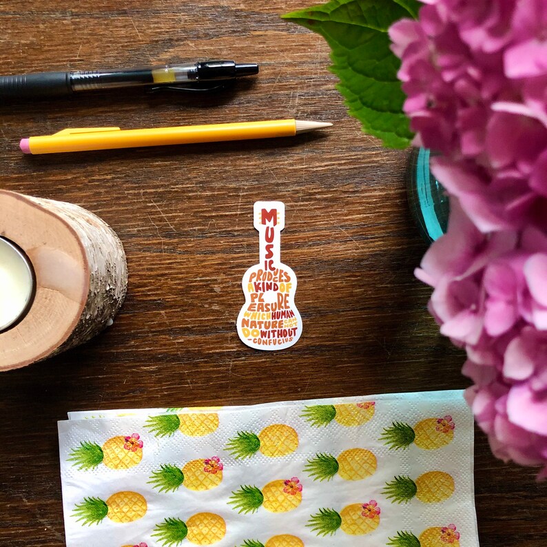 May include: A brown and yellow guitar-shaped sticker with the text "Music produces a kind of pleasure which human nature cannot do without -Confucius"