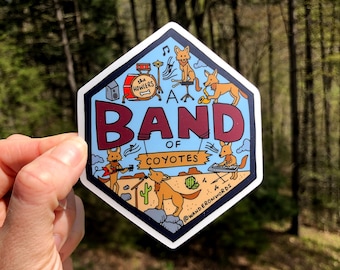 May include: A hexagonal sticker featuring a cartoon band of coyotes. The sticker has a blue background with the words "BAND of COYOTES" in maroon. The coyotes are playing various instruments, including drums, a saxophone, and a keyboard. The sticker also includes the text "the howlers" and "wanderonwords".