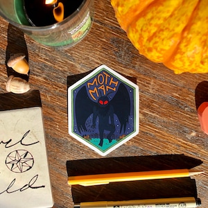 May include: A hexagonal sticker with a dark blue background and a white border. The sticker features a black mothman with red eyes, standing on a green field with a white fence. The text "Moth Man" is written in yellow letters above the mothman. The text "Est. 1967 WV" is written in white letters below the mothman.