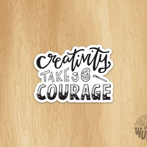 May include: Black and white sticker with the text "Creativity takes courage" in a handwritten font. The sticker is on a wood background. The text "Wander on Words" is in the lower right corner of the image.