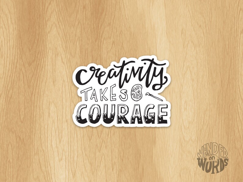 May include: Black and white sticker with the text "Creativity takes courage" in a handwritten font. The sticker is on a wood background. The text "Wander on Words" is in the lower right corner of the image.