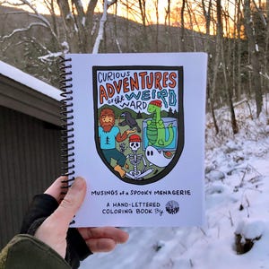 May include: A hand-lettered coloring book titled "Curious Adventures of the Weird Ward: Musings of a Spooky Menagerie" by "Wanderlust Words". The cover features a colorful illustration of a spooky menagerie inside a circle.