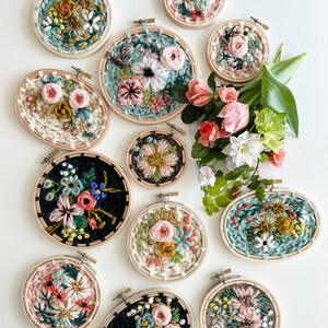 May include: A collection of 12 small embroidery hoops with floral designs. The hoops are made of wood and have a natural finish. The embroidery designs are colorful and feature a variety of flowers, leaves, and other botanical elements.