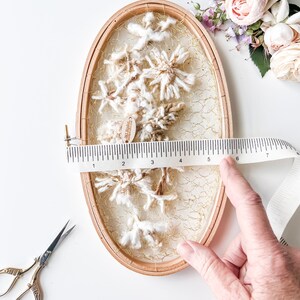 May include: A white and brown yarn wall hanging with a gold wire mesh background. The hanging is in a wooden oval hoop with a diameter of 6 inches.