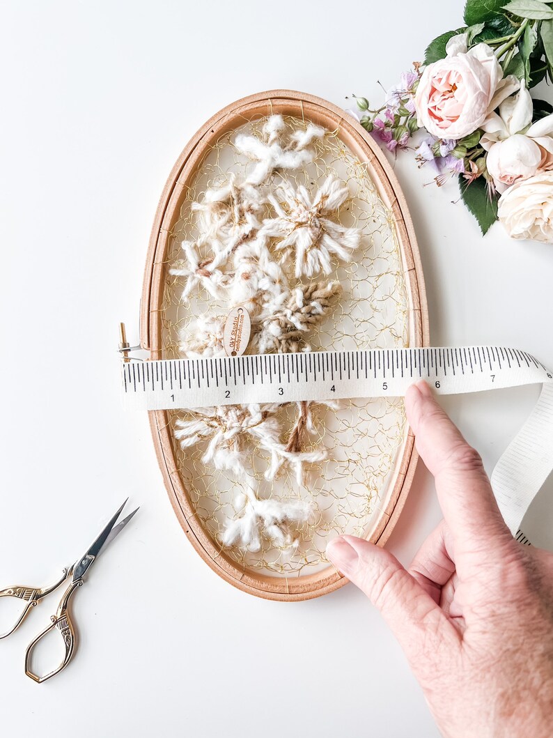 May include: A white and brown yarn wall hanging with a gold wire mesh background. The hanging is in a wooden oval hoop with a diameter of 6 inches.