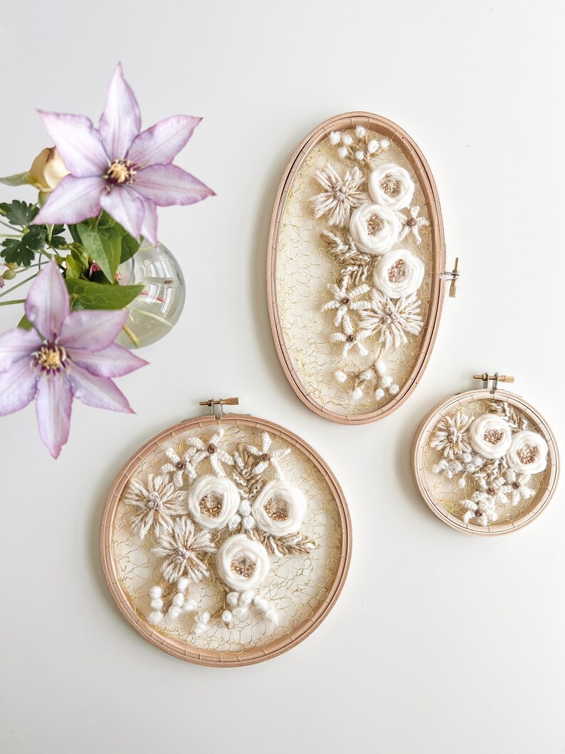 May include: Three embroidery hoops with white floral designs on a white background. The hoops are different sizes and are all framed in natural wood.