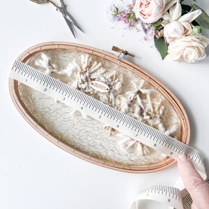 May include: A wooden embroidery hoop with a gold mesh and white yarn inside. A ruler and a measuring tape are also in the image. The tag on the yarn reads "Clay Studio Handmade with Love".
