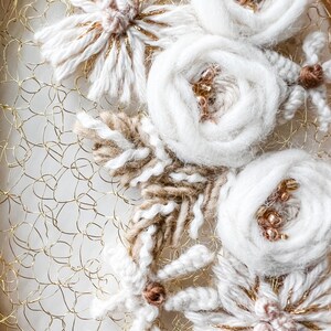 May include: A close-up of a white and gold floral embroidery on a gold wire mesh background. The embroidery features white yarn flowers with gold accents and brown yarn leaves.