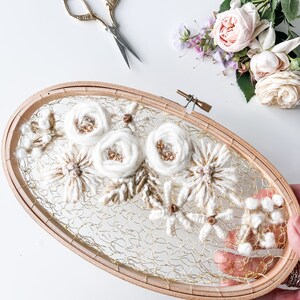 May include: A white and brown floral embroidery hoop art piece with a gold wire mesh background. The hoop is made of wood and has a natural finish.