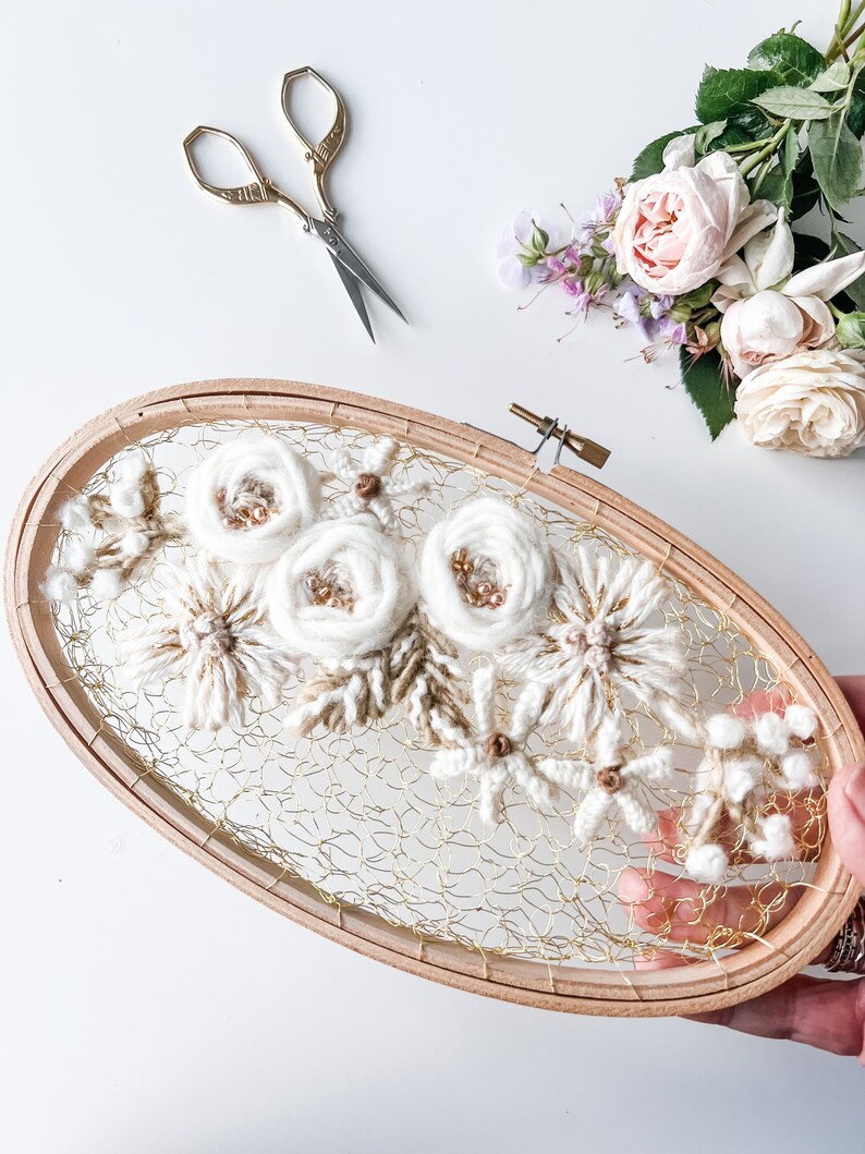 May include: A white and brown floral embroidery hoop art piece with a gold wire mesh background. The hoop is made of wood and has a natural finish.