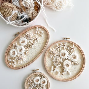 May include: Three embroidery hoops with white floral designs on a white background. The hoops are different sizes and have a gold wire mesh backing.
