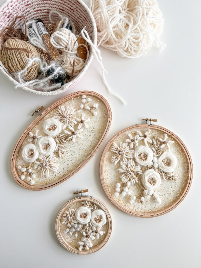 May include: Three embroidery hoops with white floral designs on a white background. The hoops are different sizes and have a gold wire mesh backing.