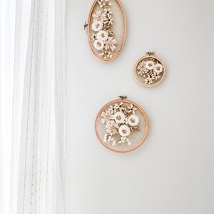 May include: Three circular embroidery hoops with dried floral arrangements. The hoops are made of wood and have a natural finish. The flowers are white and cream and are arranged in a loose, organic style.