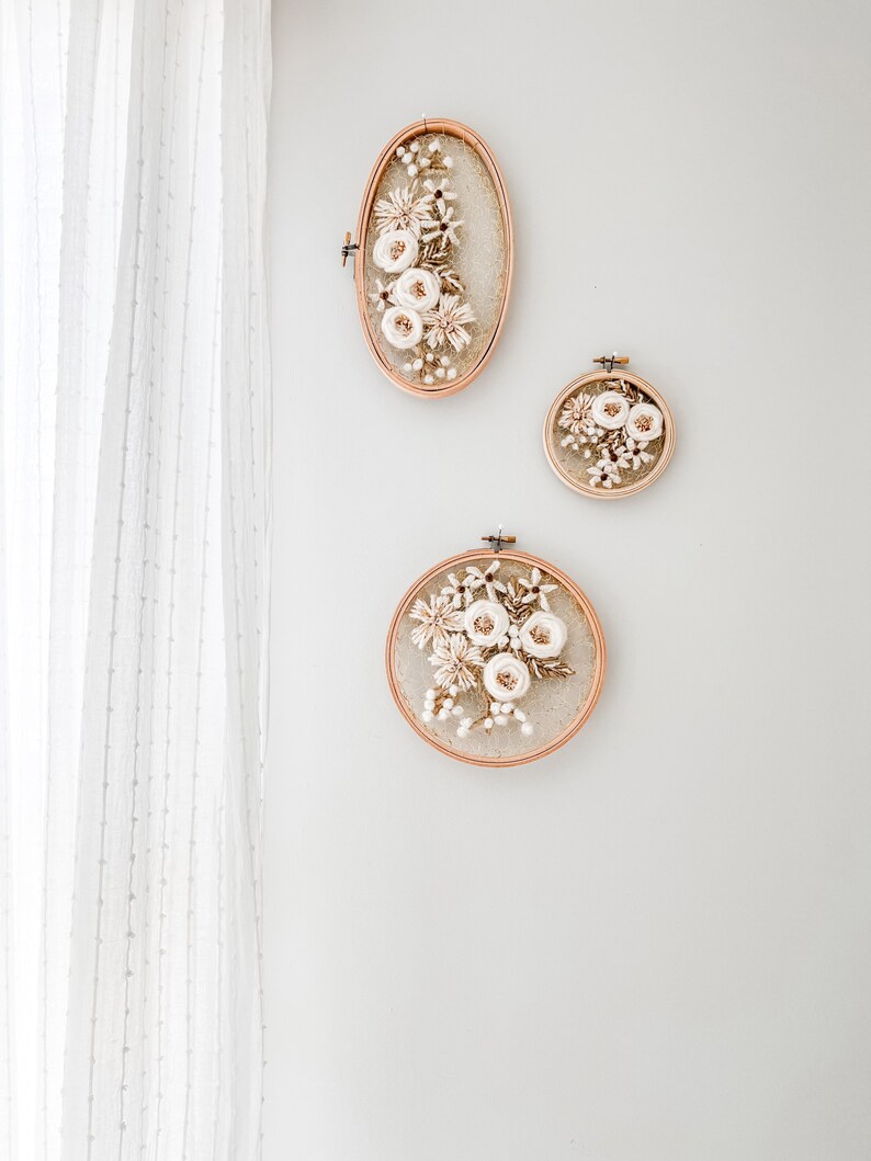 May include: Three circular embroidery hoops with dried floral arrangements. The hoops are made of wood and have a natural finish. The flowers are white and cream and are arranged in a loose, organic style.