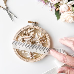 May include: A wooden embroidery hoop with a white and gold yarn design. The hoop is 4 inches in diameter and has a small tag that reads "Sky Studio - candysstudio.com".