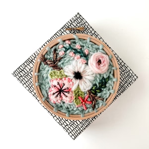 May include: A close-up of a floral embroidery hoop art piece. The hoop is made of wood and has a green fabric background. The embroidery features pink, white, and green flowers.
