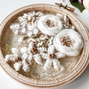May include: A white and brown wool embroidery hoop art piece with a floral design. The hoop is made of wood and has a gold wire mesh backing.