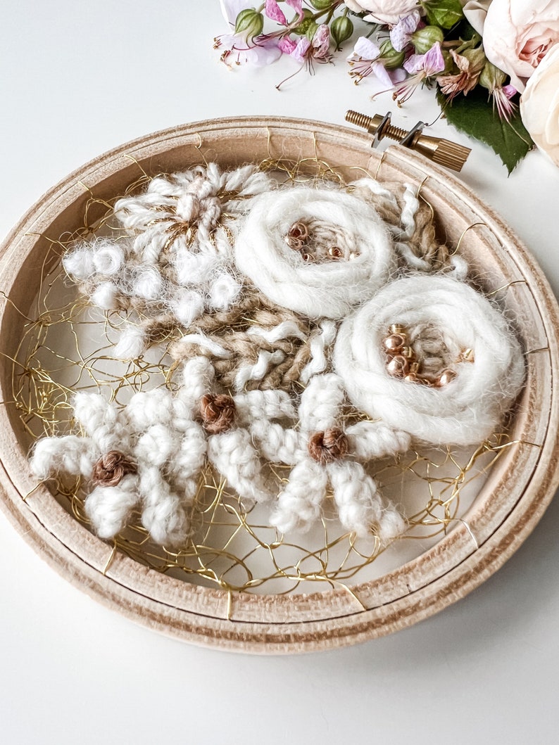 May include: A white and brown wool embroidery hoop art piece with a floral design. The hoop is made of wood and has a gold wire mesh backing.