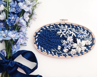 May include: A blue and white floral embroidery hoop art piece with a blue satin ribbon bow. The embroidery features a variety of blue and white flowers and leaves.