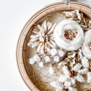 May include: A white and gold embroidery hoop art piece with a floral design. The embroidery is done with yarn and beads and is framed in a wooden hoop.