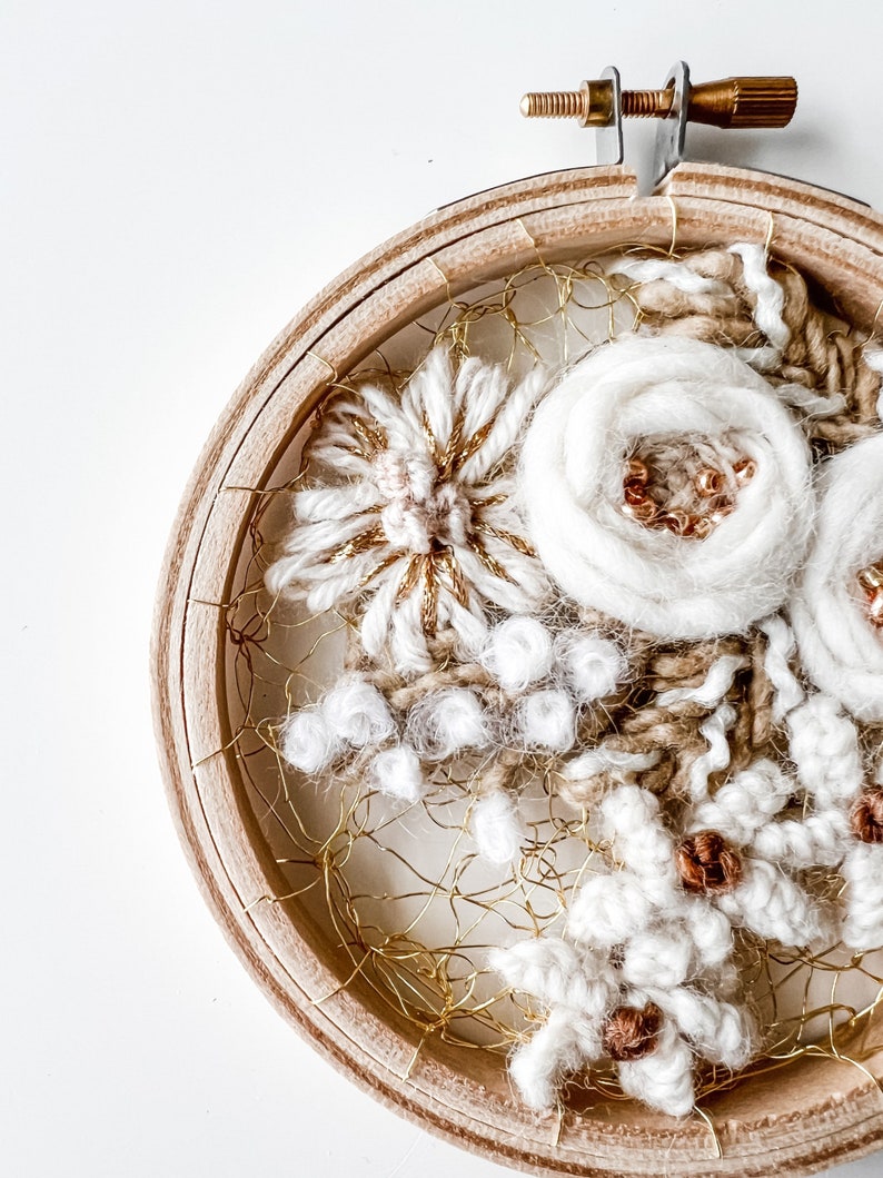 May include: A white and gold embroidery hoop art piece with a floral design. The embroidery is done with yarn and beads and is framed in a wooden hoop.