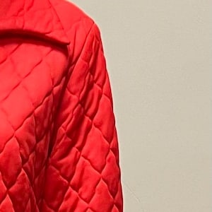 May include: A long, red quilted robe with a zipper closure. The robe has a diamond pattern and a collar.
