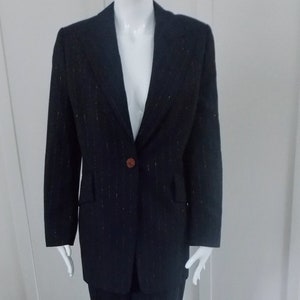 May include: A black pinstripe suit with a single button closure. The suit is on a mannequin and is standing on a black and white polka dot surface.