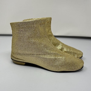 Puede incluir: Botas de tobillo de brillo dorado con punta puntiaguda y tacón bajo.