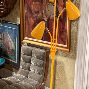 May include: A tall floor lamp featuring a central yellow metal pole that branches into three adjustable arms, each topped with a conical yellow shade. The lamp has metallic silver accents at the joints where the shades connect to the arms.