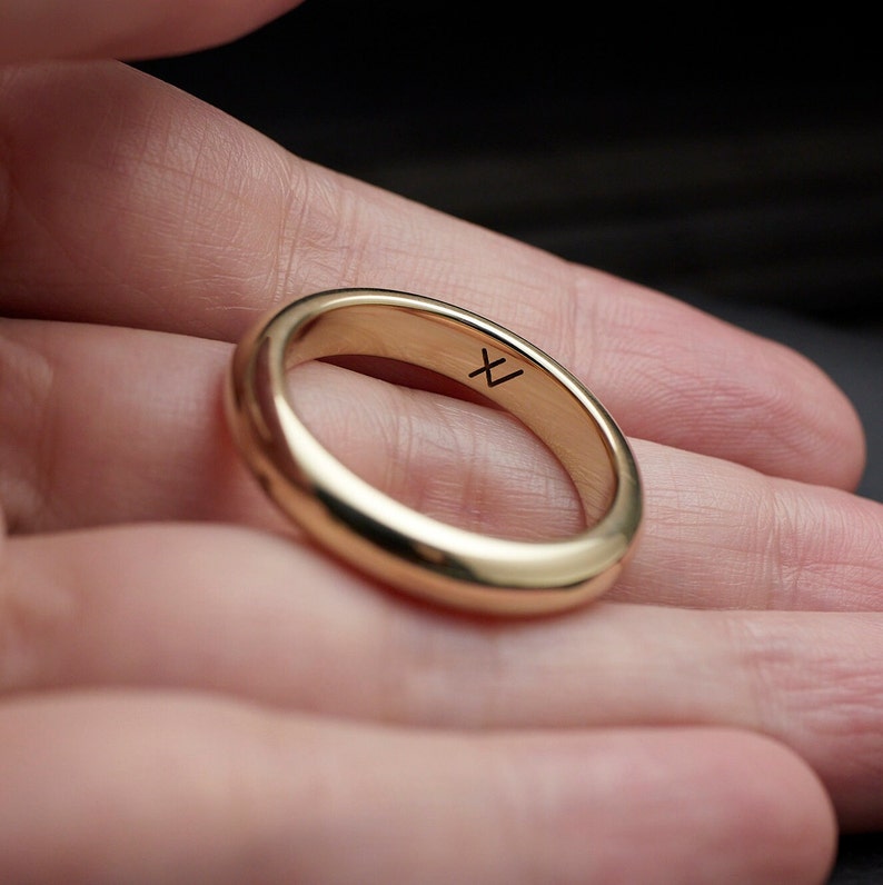 May include: A simple gold band ring with a small inscription on the inside of the band. The inscription is the letter "X".