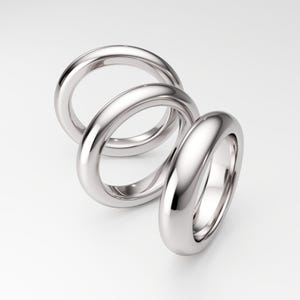 May include: Three polished silver rings arranged in a spiral. The rings have a smooth, rounded design and reflect the light, creating a bright, shiny appearance. The rings are set against a white background.