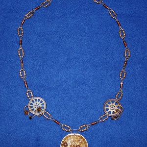 May include: A gold necklace with a brown and gold chain. The necklace has three circular pendants with gears and other metal pieces inside. The pendants are attached to the chain with small gold rings.