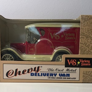 May include: A red 1923 Chevy delivery van die-cast metal coin bank with a key. The van has a white trim and says "V&S Variety Stores" on the side. The box is brown with a red stripe and says "1/25 Scale Locking Coin Bank w/Key".